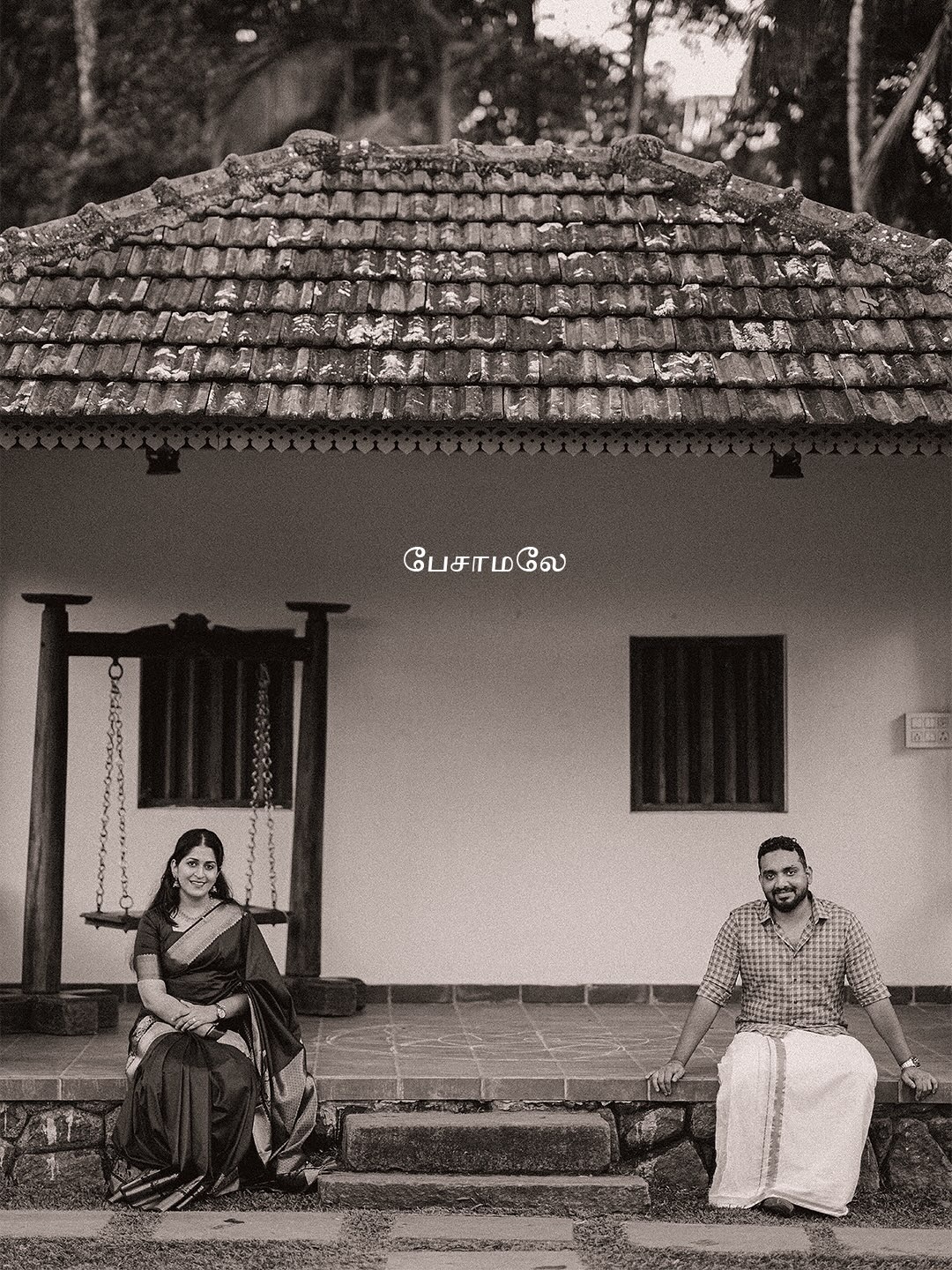 A black-and-white portrait of a couple outside a traditional home